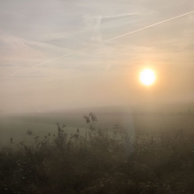 Cover art for The Third Continuum: a hazy sunrise over a misty field, seen through glass